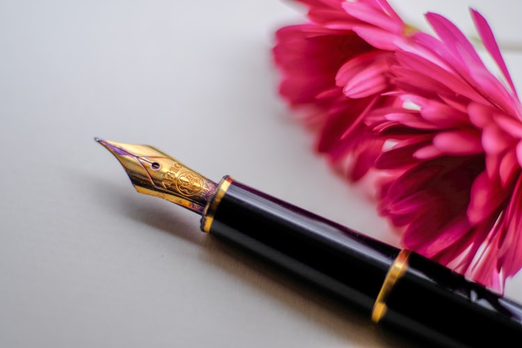 A fountain pen next to a flower that represents obituary advice from funeral comparison website Funeralocity in New Orleans, LA
