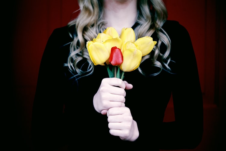Woman holding a bouquet of yellow flowers and one red flower